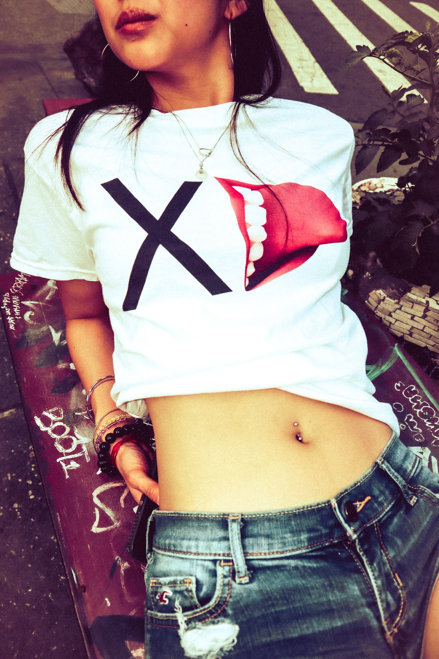 Person wearing a white t-shirt with a red and black design, standing on a street.